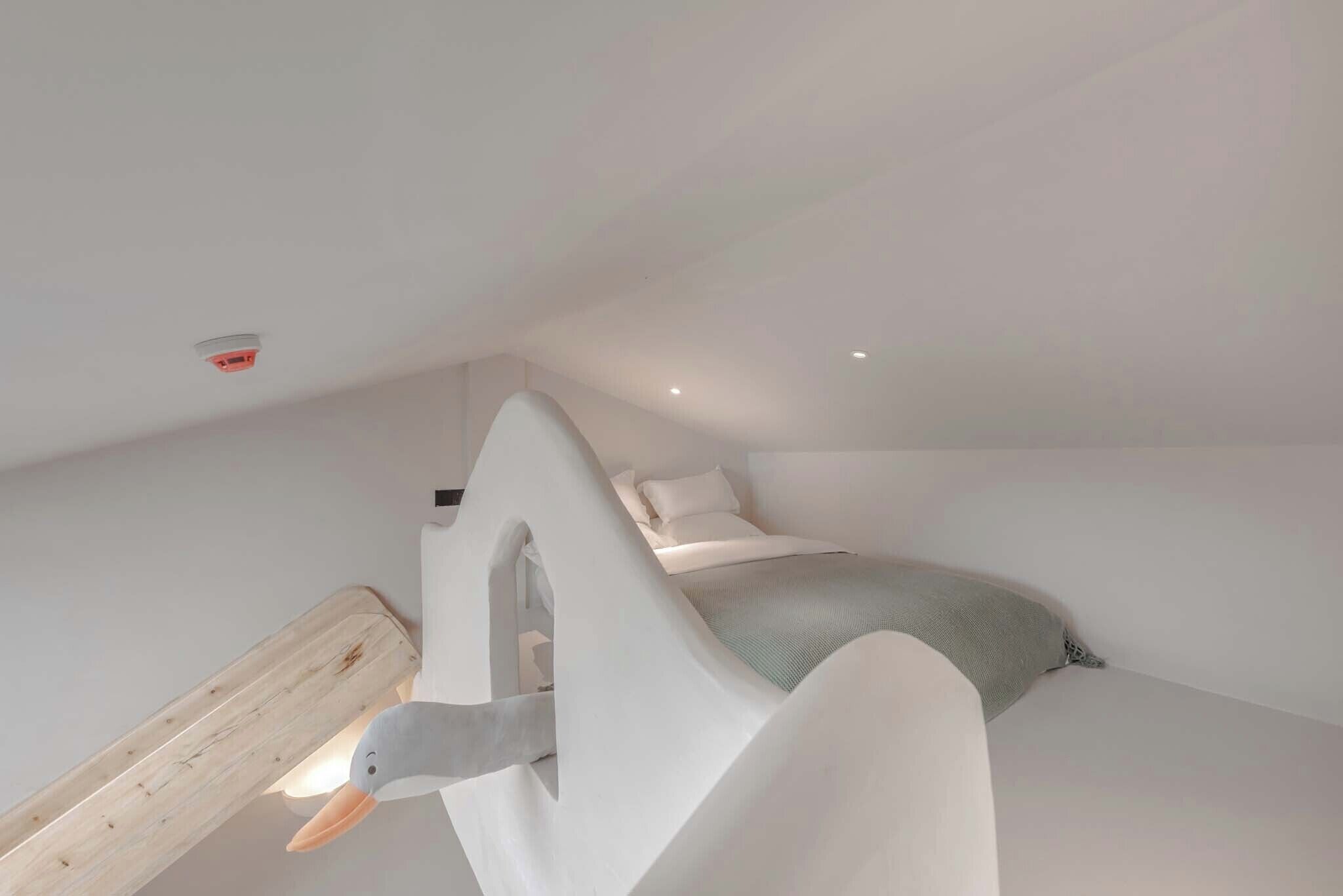 Un dormitorio moderno con un cabecero original en forma de pato, un estante de listones de madera y una cama con manta gris.