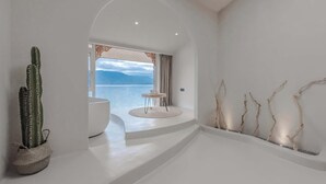 Et moderne interiør med minimalistisk design, med et stort vindue med havudsigt, en kaktusplante og et lille rundt bord.