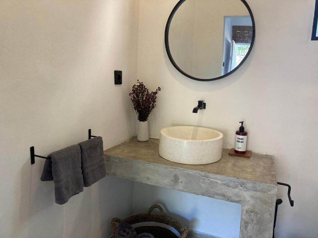 A bathroom with a round mirror, a white sink, a vase with dried flowers, and a towel rack.