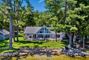 A house with a stone patio, a fire pit, and a lawn. - Luxury Otsego Lakefront. Sleeps 9.  Ski & Snowmobile (Gaylord)