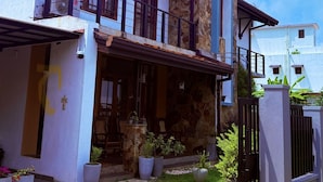 Ein zweistöckiges Haus mit Naturstein-Fassade, einem Balkon und einer überdachten Veranda mit Blumentöpfen.
