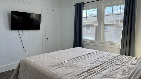 A bedroom with a bed, a TV mounted on the wall, and a window with curtains.