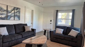 Ein Wohnzimmer mit zwei dunkelgrauen Sofas, einem Marmortisch und abstrakter Wandkunst.