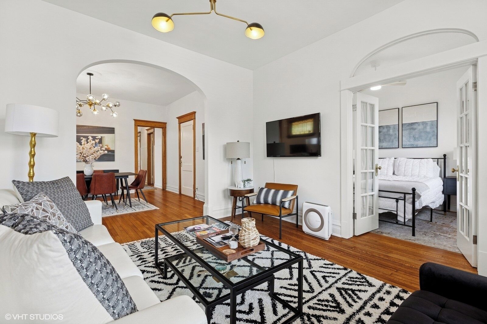 A spacious living room with a sofa, coffee table, and a TV mounted on the wall.