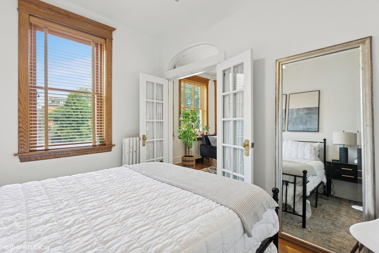 Une chambre avec un grand lit, une commode, une chaise et une fenêtre avec des stores.