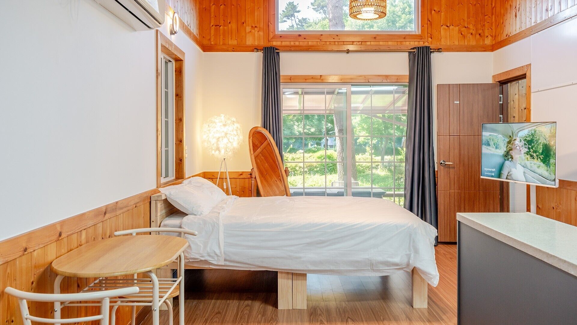 A bedroom with a bed, a desk, a chair, a television, and a window with curtains.