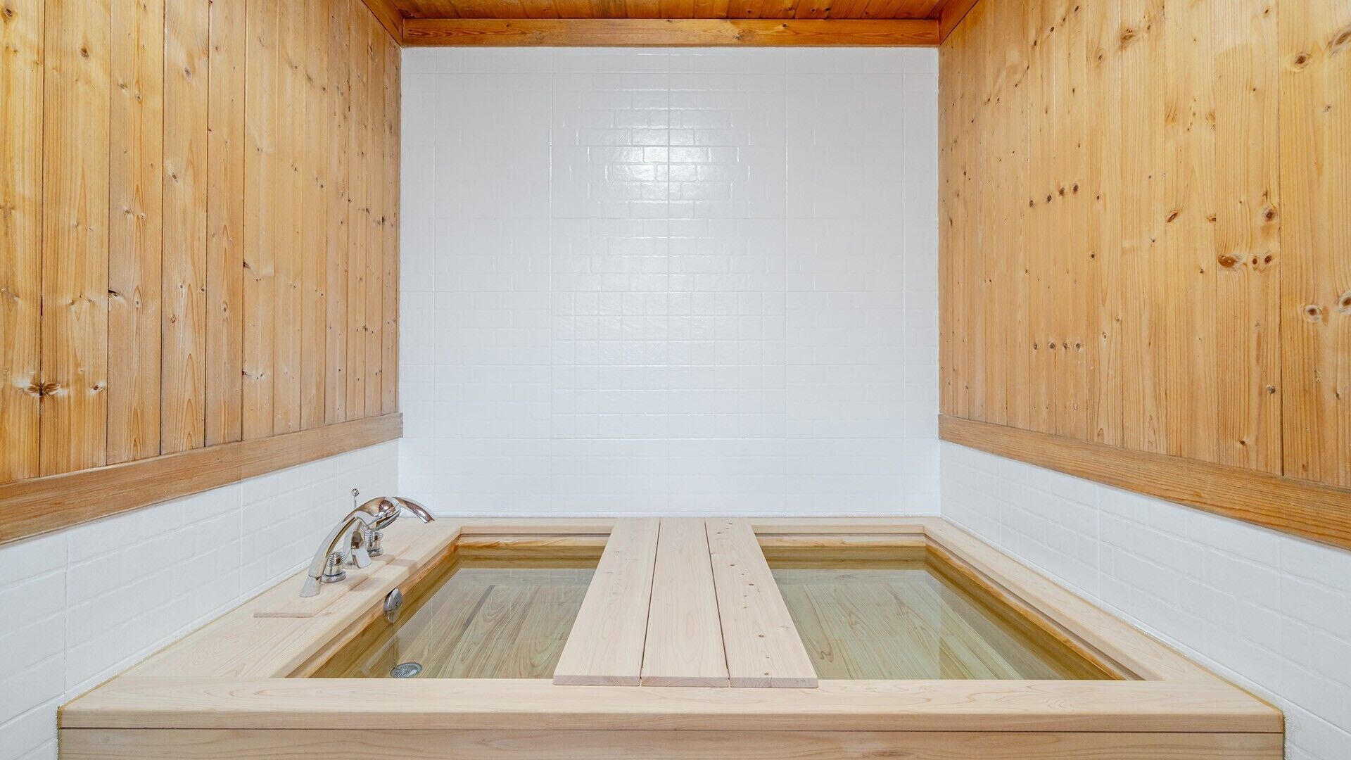 A wooden sauna with a rectangular shape, white tiled walls, and a wooden bench in the center.