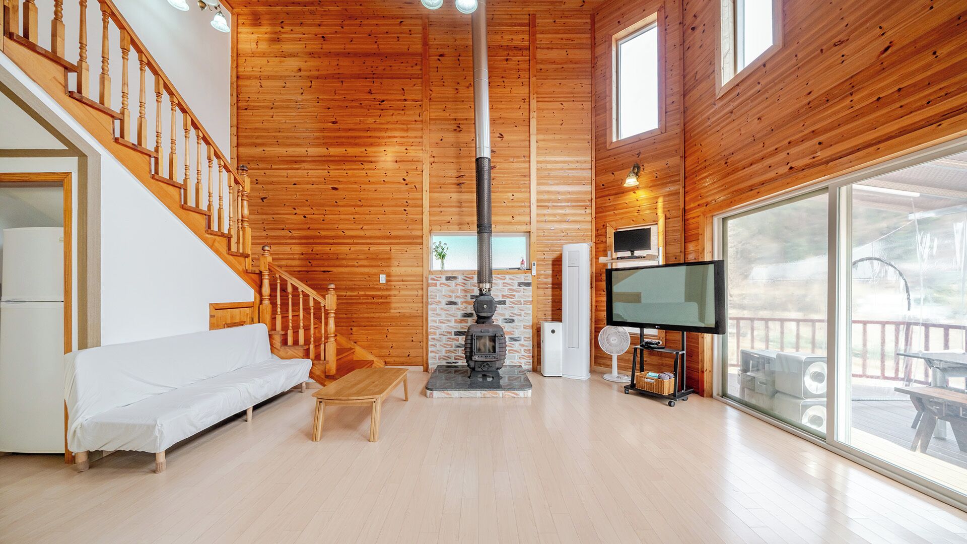 A wooden interior with a sofa, a fireplace, a TV, and a large window.