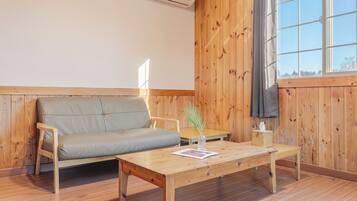 A room with a wooden wall, a sofa, a wooden table, and a window with curtains.