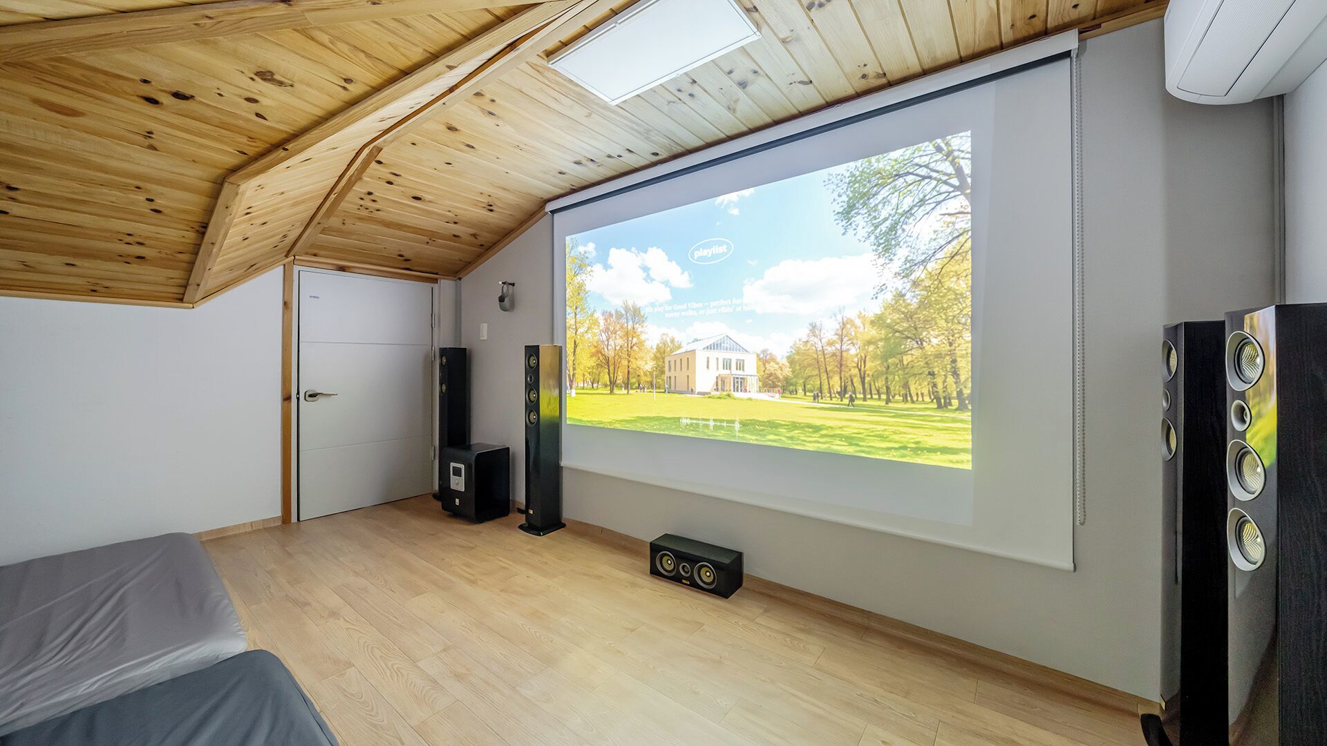 A room with a large projection screen displaying an outdoor scene, a bed, a door, and two speakers.