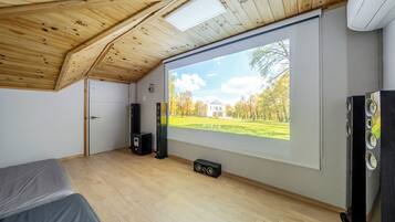 A room with a large projection screen displaying an outdoor scene, a bed, a door, and two speakers.