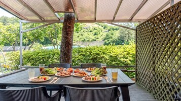Un área de comedor al aire libre con una mesa dispuesta para una comida, rodeada de sillas y vistas a un paisaje verde exuberante.