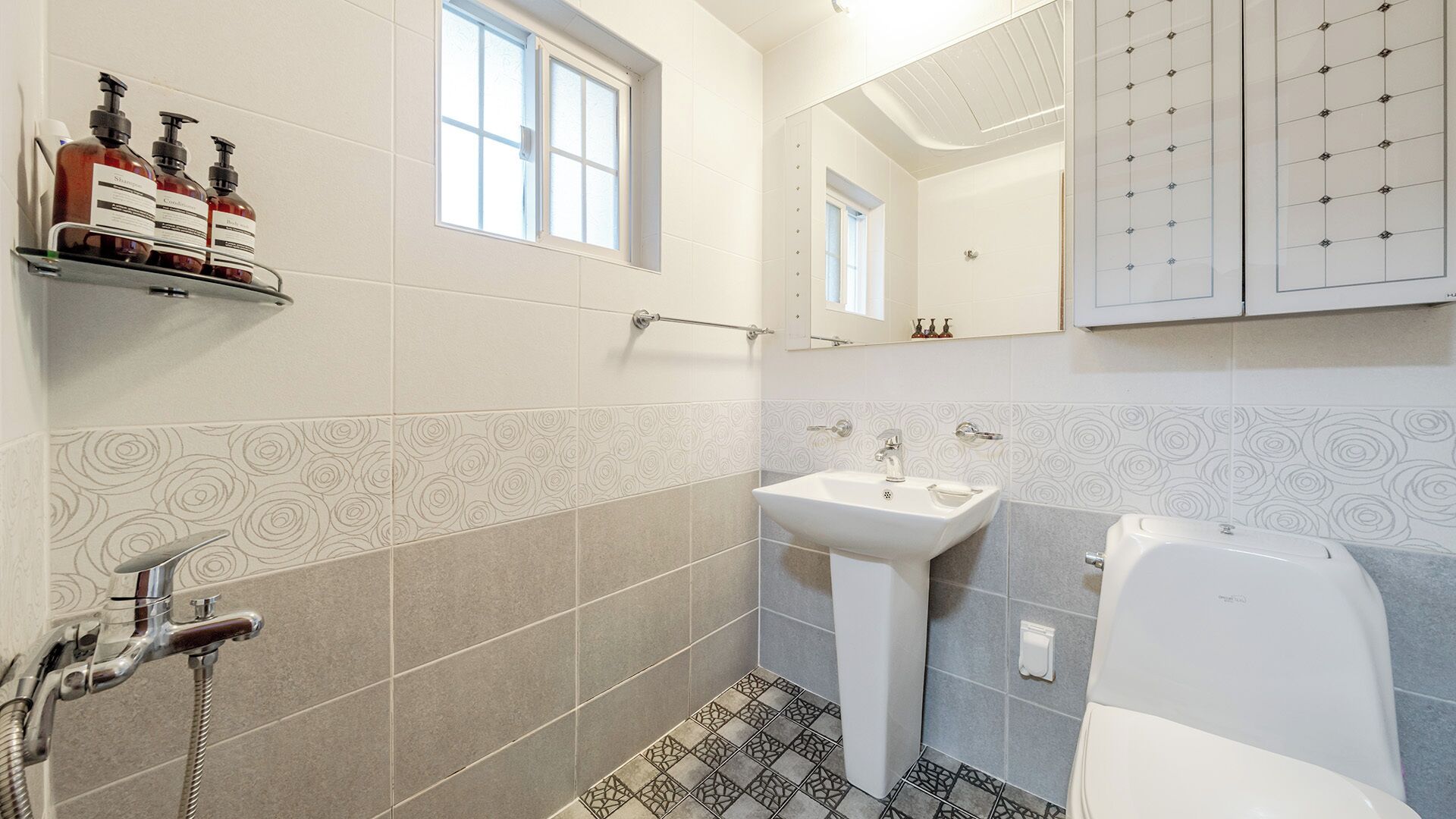 Et badeværelse med en hvid vask, et spejl og en bruser. Der er toiletartikler på en hylde.