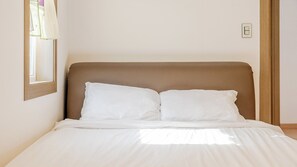 Een bed met hoofdeinde, witte beddengoed en een raam met gordijnen.