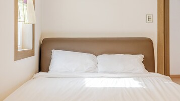 Una cama con cabecera, ropa de cama blanca y una ventana con cortinas.