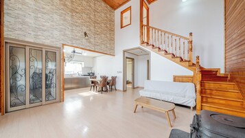 Amplia sala de estar con una escalera de madera, zona de comedor con sillas y cocina visible a través de un acceso abierto.