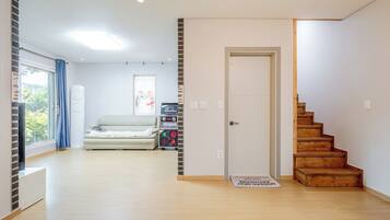 A spacious room with a wooden staircase, a sofa, a television, and a door with a window.