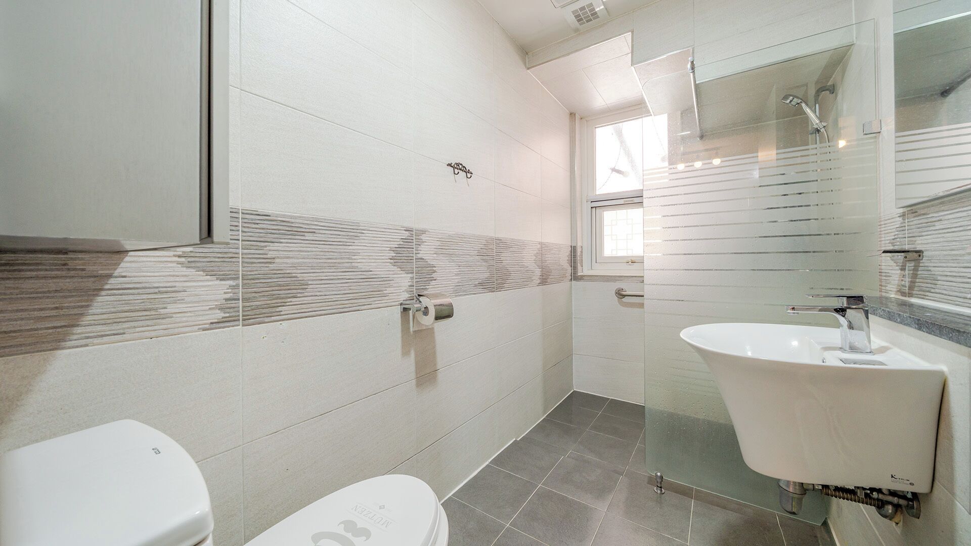 A modern bathroom with a toilet, a glass shower enclosure, and a sink with a mirror.