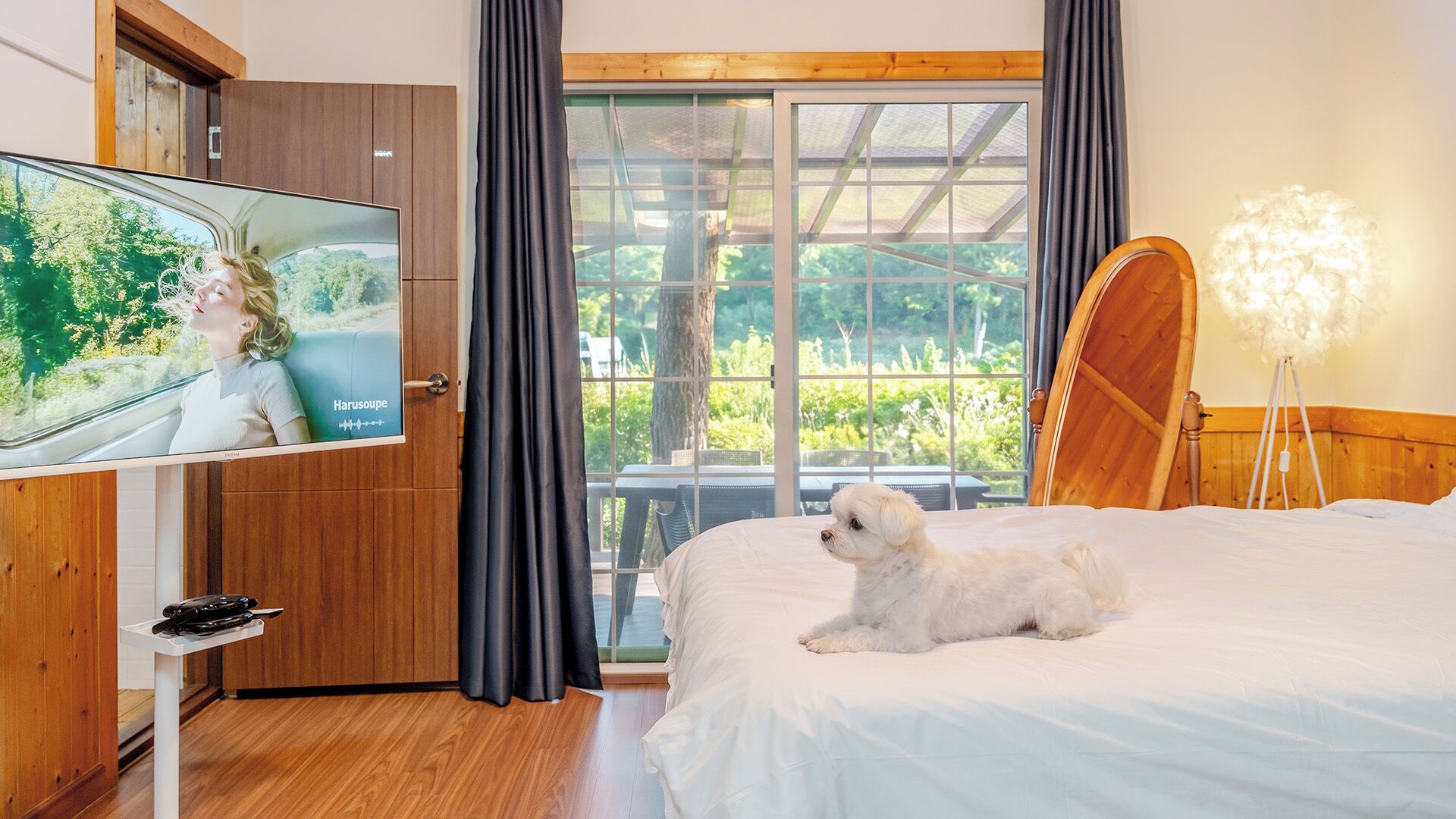 Ein Hotelzimmer mit einem Bett, einem Fernseher, einem Holzschrank, einem großen Fenster mit Vorhängen und einem kleinen Tisch.