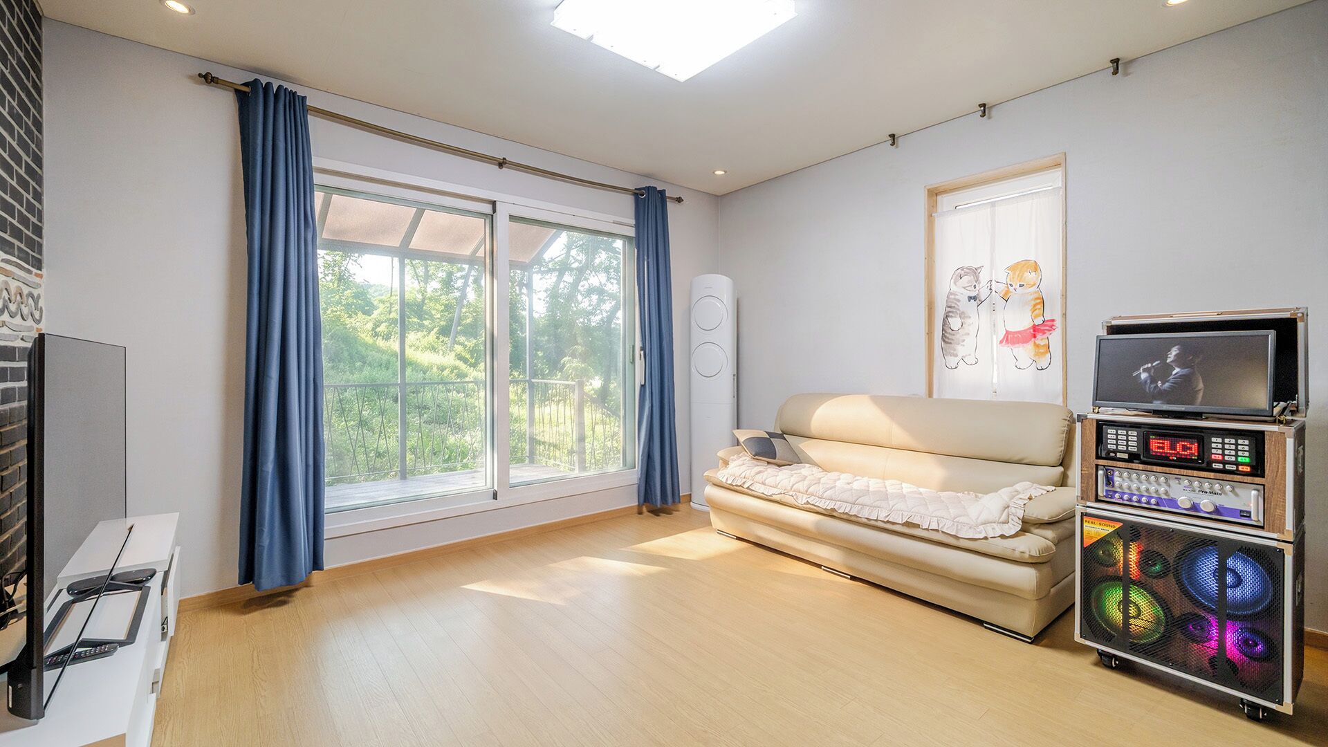 Ein Zimmer mit einer Couch, einem Fernseher, einer Stereoanlage und einem Fenster mit Vorhängen.