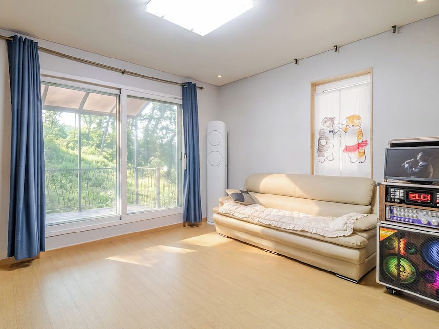 A room with a sofa, a television, a sound system, and a window with curtains.