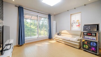 A room with a sofa, a television, a sound system, and a window with curtains.