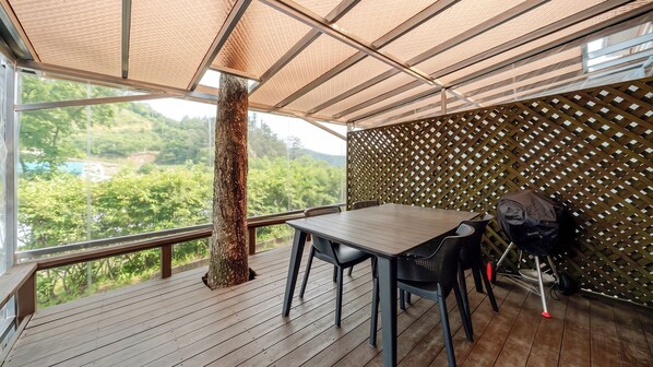 Terraza al aire libre con una mesa y sillas, el tronco de un árbol y vistas a un área boscosa.