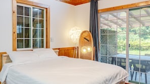 Ein Schlafzimmer mit einem Bett, einem Fenster mit Vorhängen, einer Wandleuchte und Blick ins Freie.