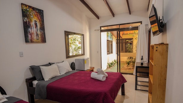 A hotel room with two beds, a painting, a TV, and a sliding glass door to the outside.