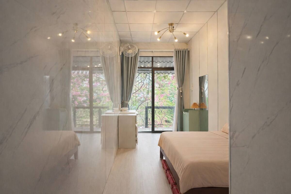 Une chambre à coucher avec un lit, une table de chevet, un miroir et une fenêtre avec des rideaux.