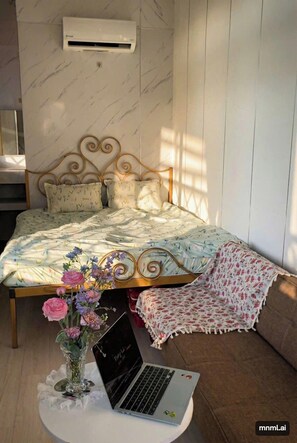 A bedroom with a bed, a laptop on a small table, and a vase with flowers. - Soluna Pearl Villa Tien Loi Residence  (Phan Thiet)