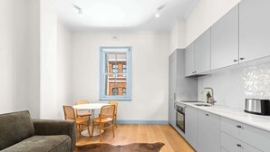 Une cuisine de taille réduite avec des meubles gris, un plan de travail blanc et une fenêtre donnant sur un immeuble en briques.