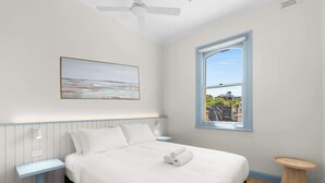 Une chambre à coucher avec un lit, une fenêtre donnant sur un beau paysage, un ventilateur de plafond et un tableau accroché au mur.