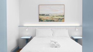 Een slaapkamer met een bed, witte kussens, nachtkastjes en een schilderij aan de muur.