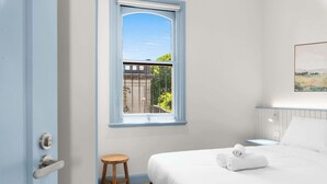 Ein Schlafzimmer mit Bett, Fenster, Tür und Hocker.