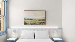 Ein Schlafzimmer mit einem Bett, zwei Nachttischen, einem Fenster und einem Bild an der Wand.