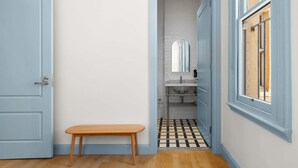 Ein Badezimmer mit gefliestem Boden, einem Waschbecken, einem Spiegel und einer Sitzbank.
