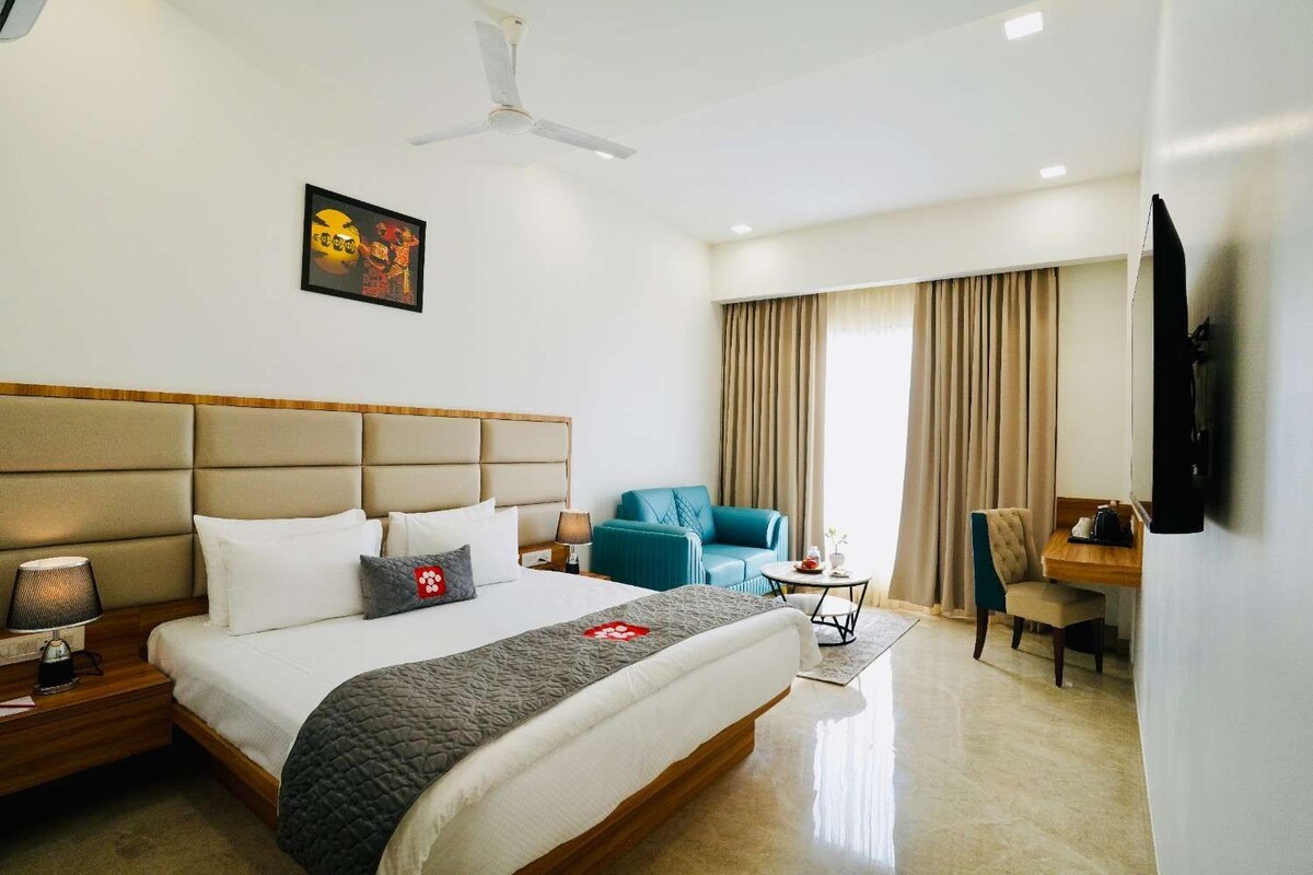 A hotel room with a bed, a desk, a chair, a sofa, a television, and a ceiling fan.