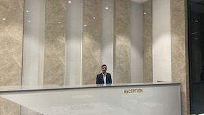 A reception desk with a marble wall background and a person standing behind it. - Mastiff Select Aparajita (Danta Ramgarh)