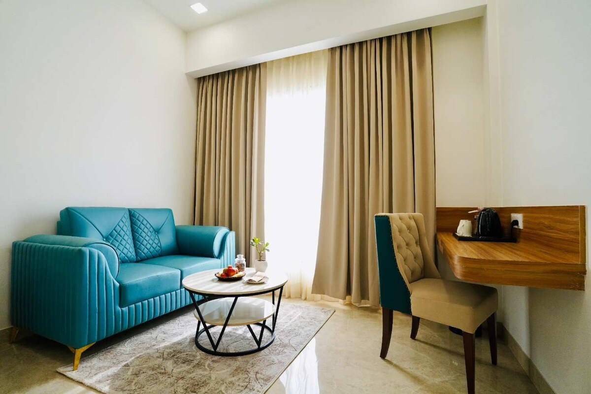 Un salon moderne avec un canapé de couleur turquoise, une table basse ronde, une table d’appoint en bois avec une bouilloire et un fauteuil.