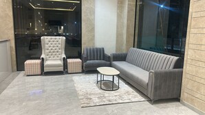 A modern living room with a tufted armchair, a grey sofa, and a small round table. - Mastiff Select Aparajita (Danta Ramgarh)