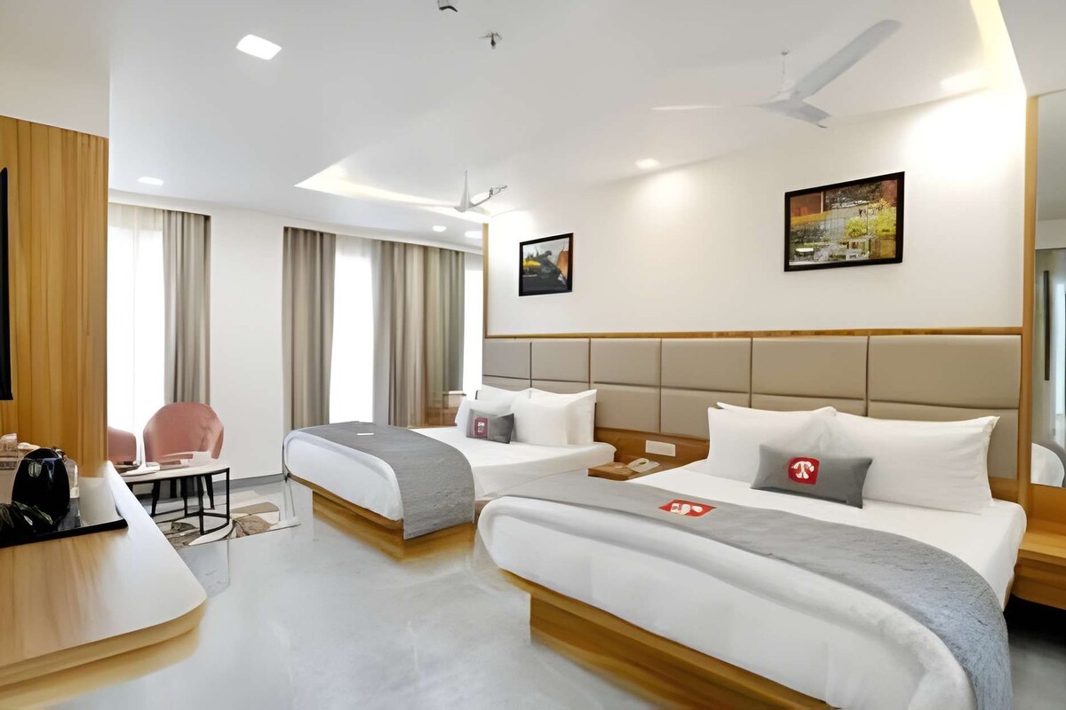 A hotel room with two beds, a desk, a chair, a TV, and a ceiling fan.