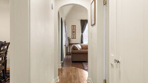 Un pasillo que conduce a una sala de estar con un sofá de cuero marrón, un tapete estampado y un cuadro en la pared.