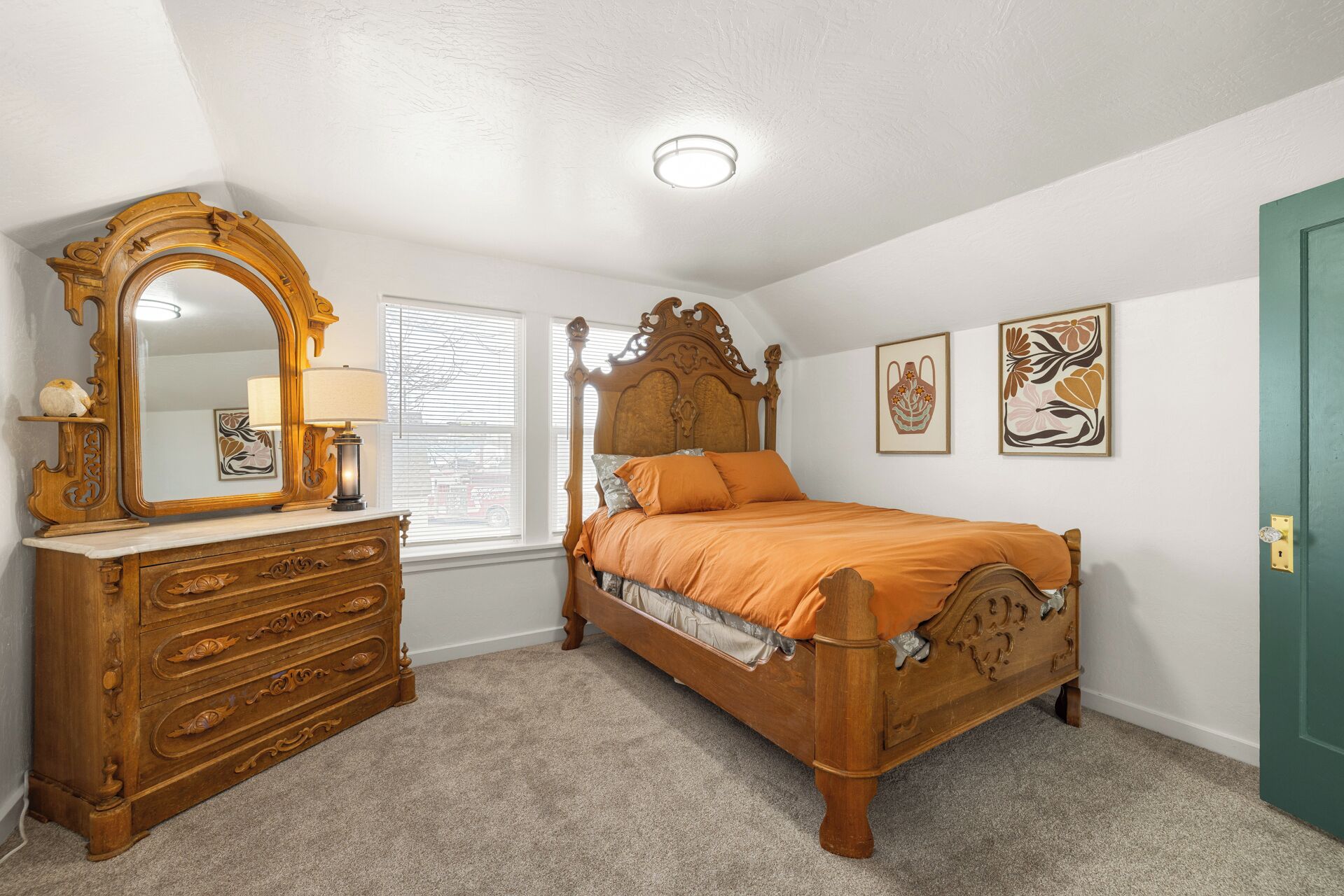Un dormitorio con cama de madera, cómoda con cajones, espejo grande y dos cuadros en la pared.