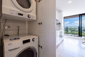 A modern laundry room with a Haier washing machine, a dryer, and a large window overlooking a balcony with a view of greenery. - Nice City Studio with Ponsonby View (Auckland City)