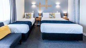 A hotel room with two beds, a sofa, and a wall with a welcome sign. - Kings Court Motel (Whanganui)