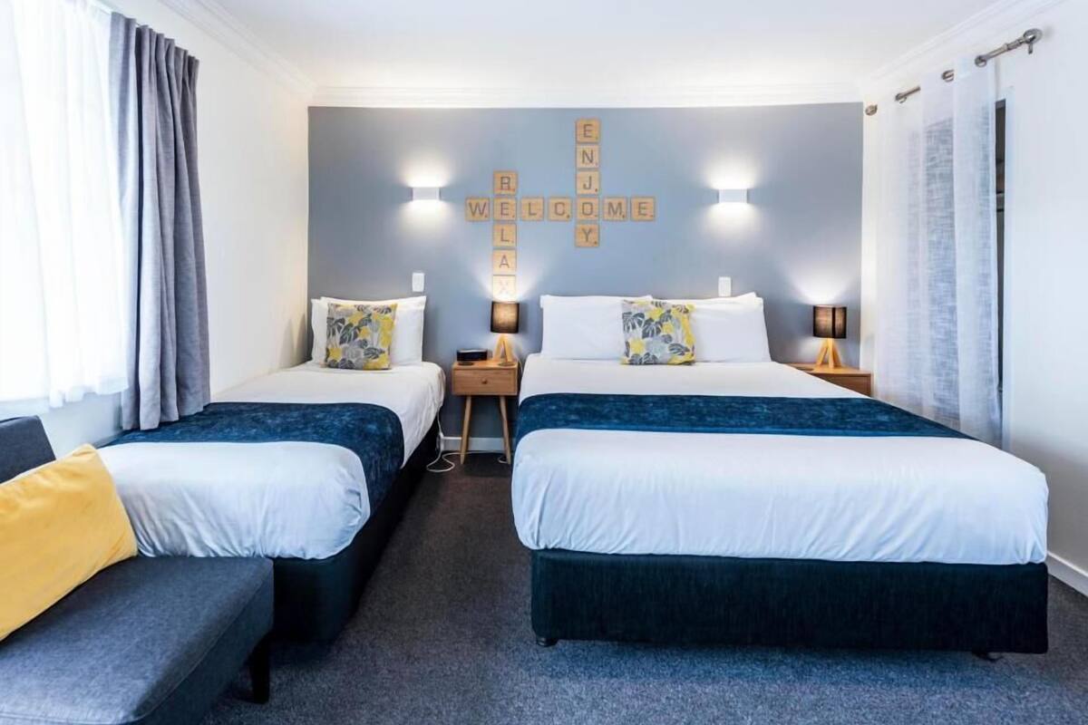 A hotel room with two beds, a sofa, and a wall with a welcome sign.