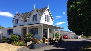 A two-story house with a porch, a driveway, and a red car parked in the background. - Kings Court Motel (Whanganui)