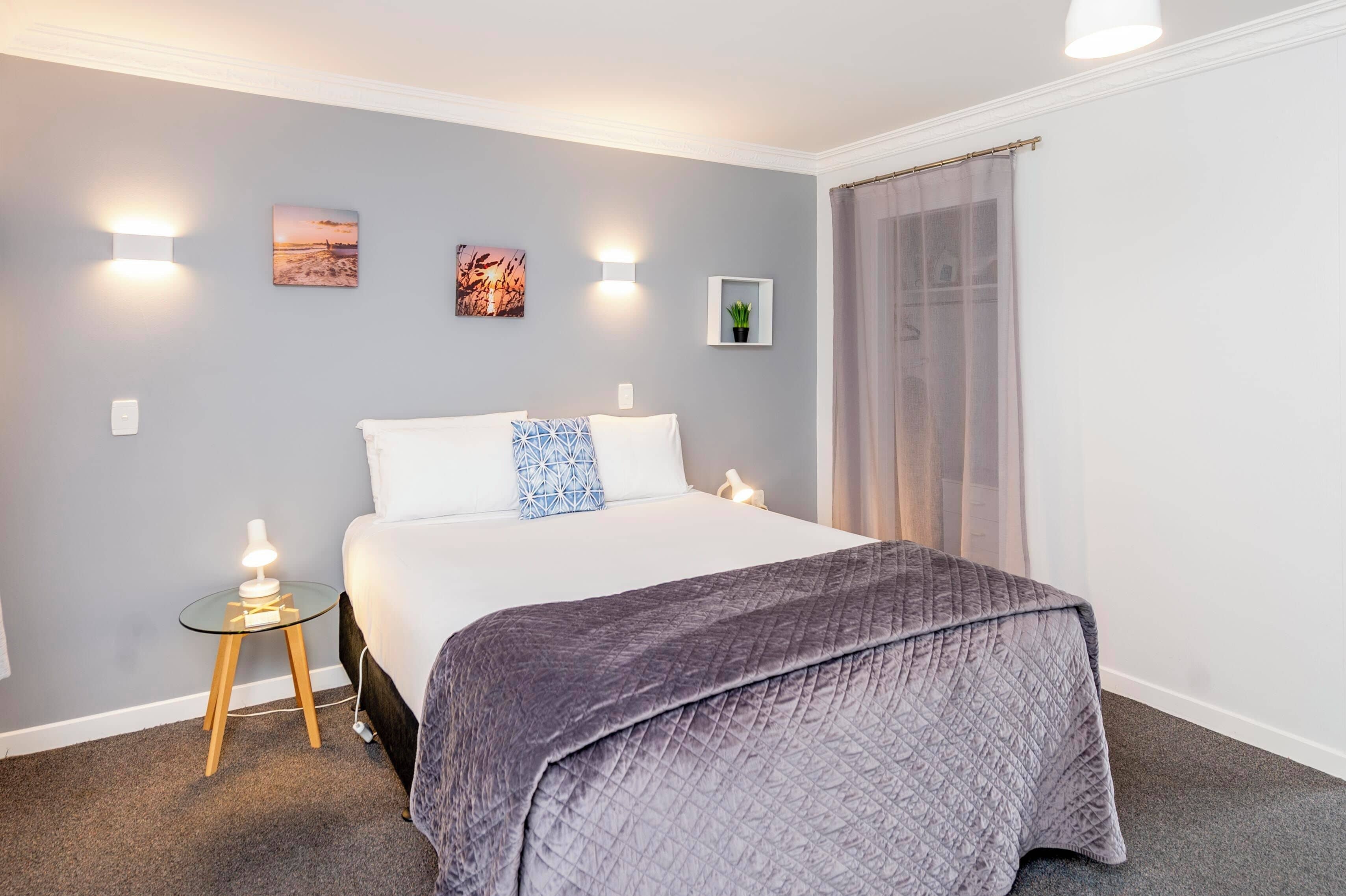 Una camera da letto ordinata con un letto, comodini, luci a parete e quadri appesi.