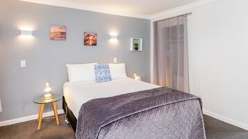 Una camera da letto ordinata con un letto, comodini, luci a parete e quadri appesi.